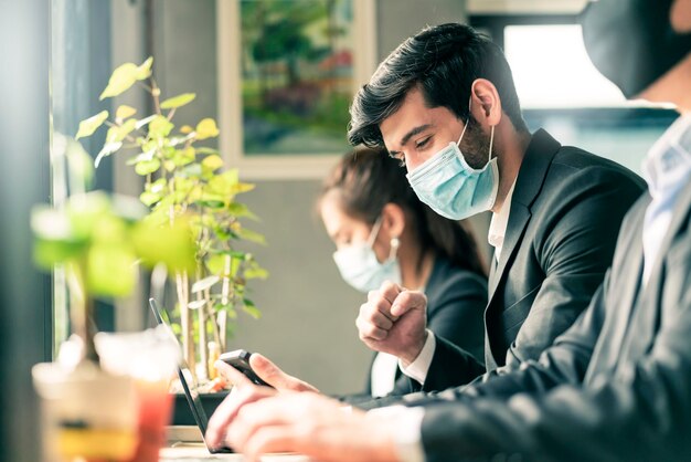 Nieuw normaal levensstijlconcept zakenmensen die een masker dragen, zitten met sociale afstand werken in de openbare ruimte of co-werkruimte met laptop en smartphone