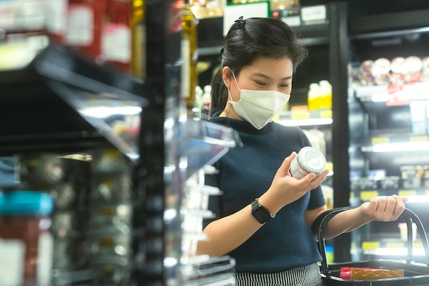 Nieuw normaal na covid-epidemie jonge slimme aziatische vrouw winkelen nieuwe levensstijl in supermarkt met gezichtsschild of maskerbescherming hand kiezen consumentenproducten nieuwe normale levensstijl