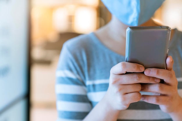 Nieuw normaal na covid19 epidemie slimme Aziatische vrouwelijke slijtage beschermingsmasker hand gebruik smartphone communicatie in warenhuis nieuwe levensstijl abstracte achtergrond wazig