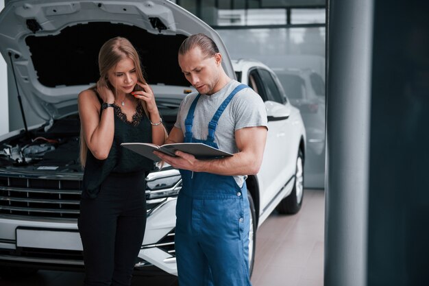 Nieuwe apparatuur nodig. Resultaten van reparatie. Zelfverzekerde man die laat zien wat voor schade haar auto is aangericht