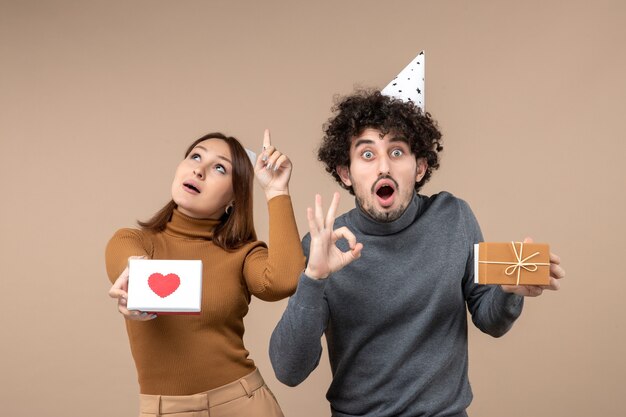 Nieuwjaar fotograferen met jong koppel dragen Nieuwjaar hoed meisje met hart omhoog en man met cadeau bril gebaar maken