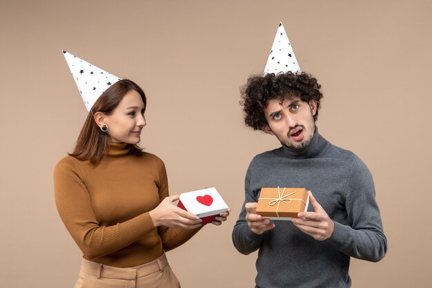 Nieuwjaar fotograferen met jong koppel dragen nieuwjaarshoed romantisch meisje met hart en man met cadeau op grijs