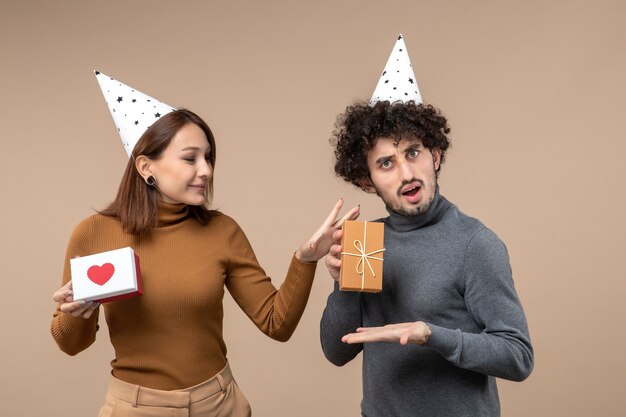 Nieuwjaar fotograferen met verrast jong koppel draagt nieuwjaarshoed meisje met hart en man met cadeau op grijs