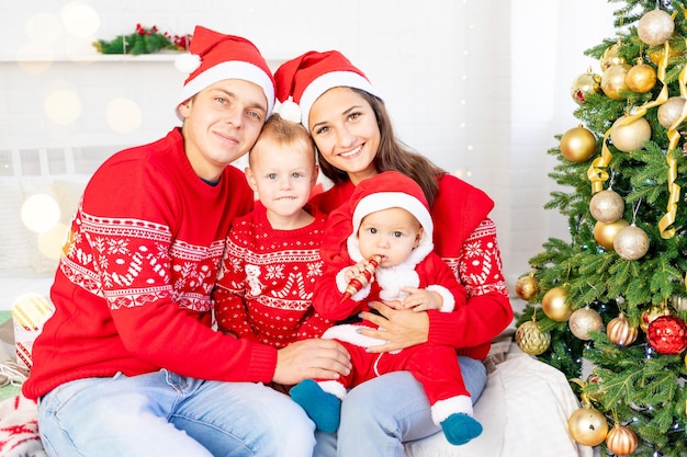Nieuwjaar of kerstmis, een gelukkig gezin met twee kinderen op het bed thuis bij de kerstboom in rode truien glimlachen, knuffelen en zoenen feliciteren met de vakantie