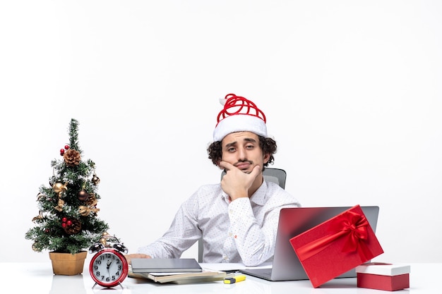 Nieuwjaarsstemming met brainstormen jonge zakenman met grappige Kerstmanhoed die diep in het bureau op witte achtergrond denken