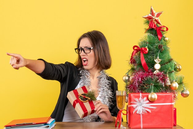 Nieuwjaarsstemming met mooie zakelijke dame in pak met bril iets te wijzen en zittend aan een tafel op kantoor