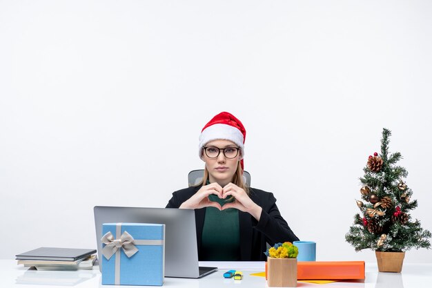 Nieuwjaarsstemming met romantische vrouw met een kerstman hoed zittend aan een tafel met een kerstboom en een cadeau erop op witte achtergrond