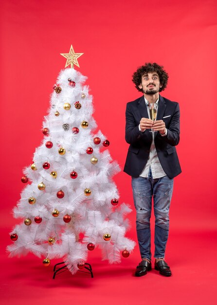 Nieuwjaarsviering met jonge man die een glas wijn geeft en dichtbij verfraaide witte kerstboom staat