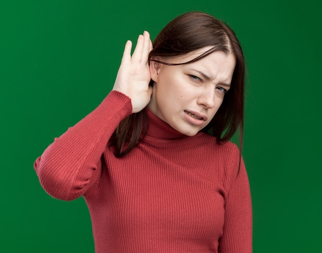 Gratis foto nieuwsgierig jong mooi meisje doet ik kan je gebaar niet horen geïsoleerd op groene muur