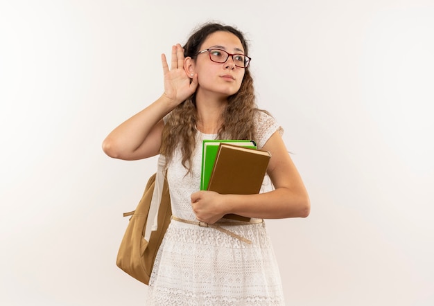 Nieuwsgierig jong mooi schoolmeisje met bril en achterzak met boeken doen kan je niet horen gebaar kijken naar kant geïsoleerd op wit met kopie ruimte