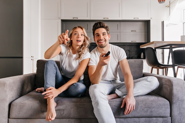 Nieuwsgierig paar zittend op een grijze bank. indoor portret van man en vrouw tv kijken.