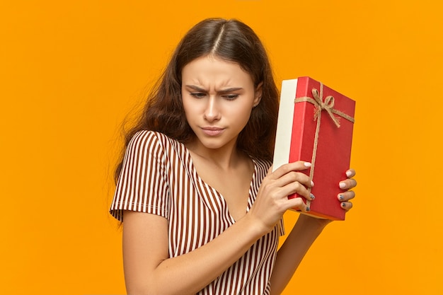 Nieuwsgierig schattig meisje in mooie gestreepte jurk met doos met gouden lint