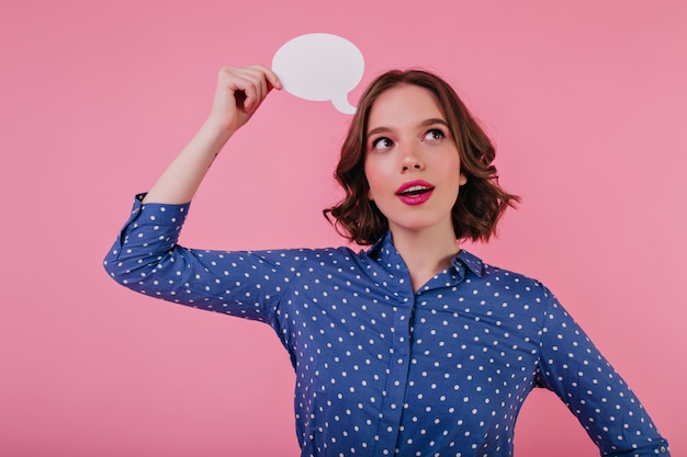 Gratis foto nieuwsgierige charmante dame in blauwe blouse poseren met zachtjes glimlach. vrolijk kaukasisch meisje dat over iets op roze muur denkt.