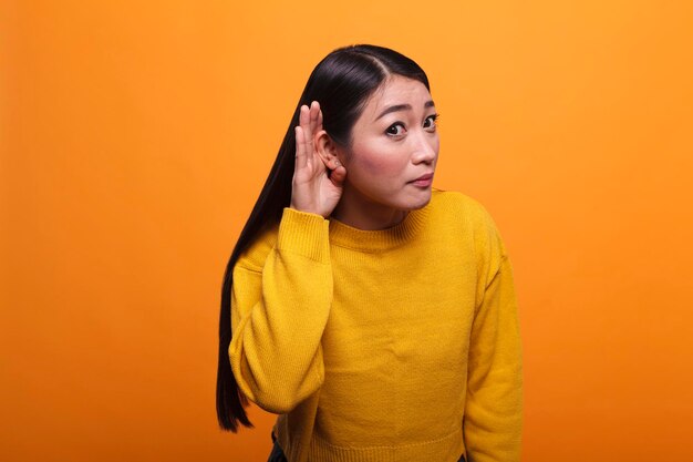 Nieuwsgierige donkerbruine aziatische vrouw die interessante roddels en geheime geruchten over haar afluistert. Geïntrigeerde serieuze persoon met de hand aan het oor die mensen hoort roddelen met interesse.