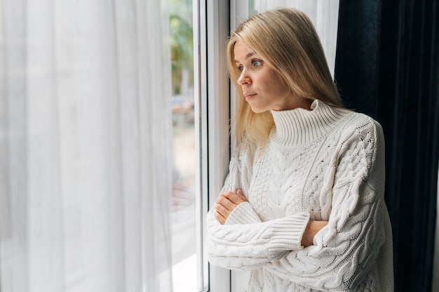 Gratis foto nieuwsgierige vrouw thuis tijdens de pandemie die door het raam kijkt