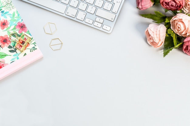 Notebook, een wit toetsenbord en roze rozen op een wit oppervlak