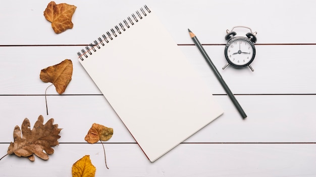 Notebook en potlood in de buurt van bladeren en wekker