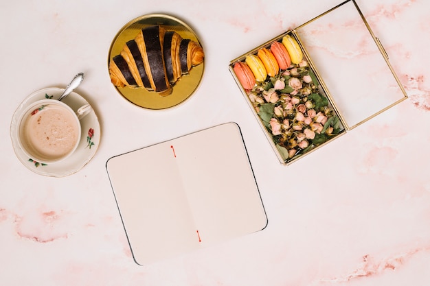 Notitieboekje met croissant en doos met bloemen op lijst