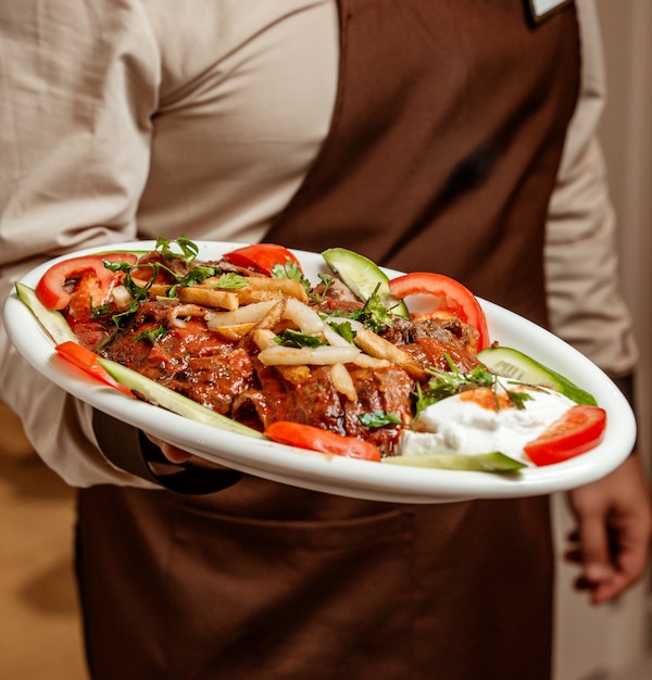 Ober die een schotel van iskenderkebab houden die met yoghurt en plantaardige plakken wordt gediend