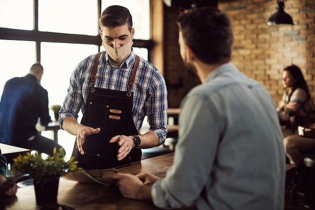 Ober draagt gezichtsmasker terwijl hij met een klant in een café praat