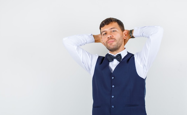 Ober hand in hand achter hoofd in shirt, vest en op zoek naar zelfverzekerd, vooraanzicht.