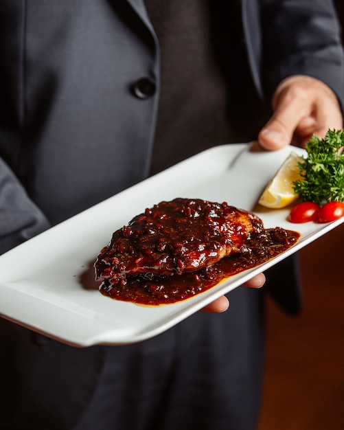 Ober met gebakken visfilet plaat bedekt met granaatappelsaus