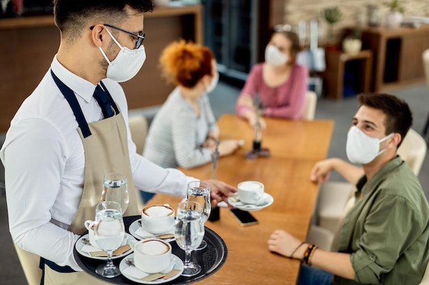 Ober serveert koffie aan klanten terwijl hij een gezichtsmasker draagt vanwege de covid19-epidemie
