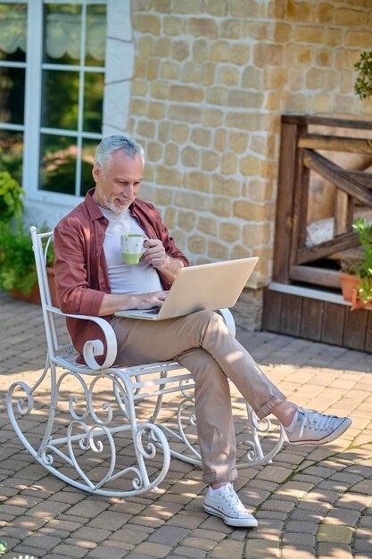 Ochtend thuis. Grijsharige man zit in een fauteuil en leest iets online