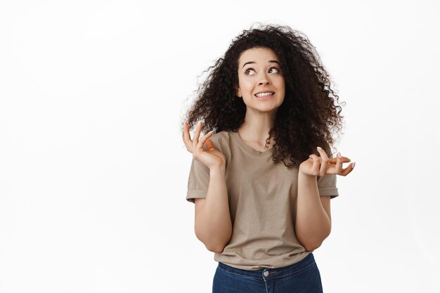 Oeps mijn domme fout. schattig onhandig krullend meisje schouderophalend, onhandig glimlachen en oogcontact vermijdend, schuldig zijn en zich verontschuldigen, sorry zeggen, staande op een witte achtergrond