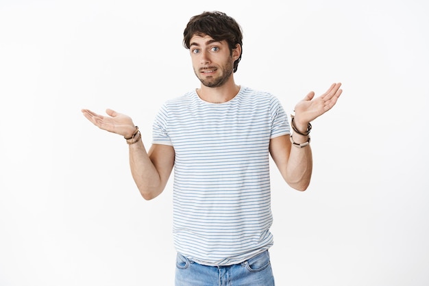 Oeps sorry. Onhandige en intense jonge aantrekkelijke man met borstelharen en blauwe ogen die schuldig glimlachen terwijl hij zijn schouders ophaalde met gespreide handen en een fout maakte, zich verontschuldigend omdat hij geen idee had hoe het gebeurde.