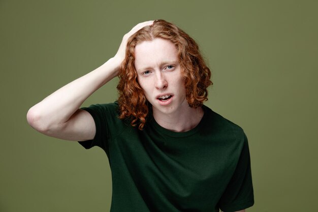 onaangenaam greep het hoofd van een jonge knappe man met een groen t-shirt geïsoleerd op een groene achtergrond