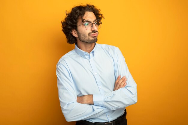 Onaangename jonge knappe blanke man met bril permanent met gesloten houding kijken naar kant geïsoleerd op een oranje achtergrond met kopie ruimte