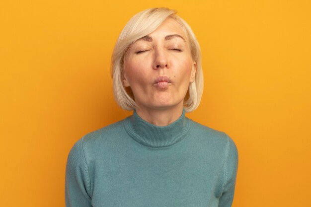 Onaangename mooie blonde Slavische vrouw die zich met gesloten ogen bevindt die op oranje muur wordt geïsoleerd