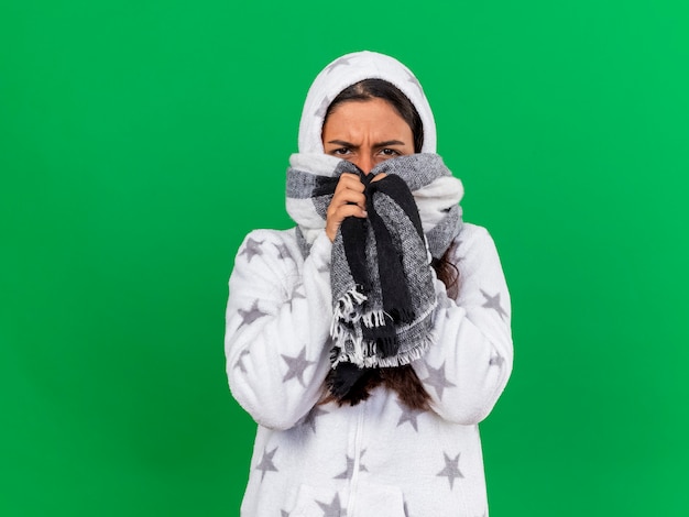 Gratis foto onbehaagd jong ziek meisje die op kap wearin sjaal bedekt gezicht met sjaal zetten die op groene achtergrond wordt geïsoleerd