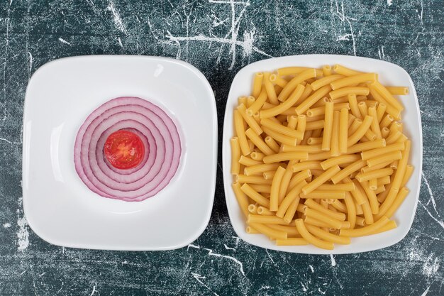 Onbereide verse macaroni met plakjes ui en tomatenkers.