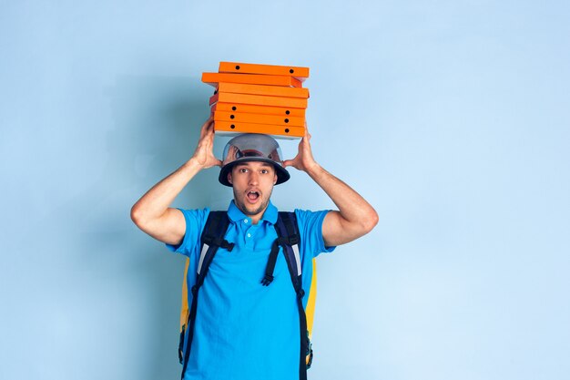 Onberispelijke bezorgservice tijdens quarantaine. Man levert voedsel en boodschappentassen tijdens isolatie. Emoties van bezorger die op blauw worden geïsoleerd