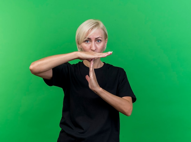 Onder de indruk blonde Slavische vrouw van middelbare leeftijd die time-outgebaar doet dat op groene muur met exemplaarruimte wordt geïsoleerd