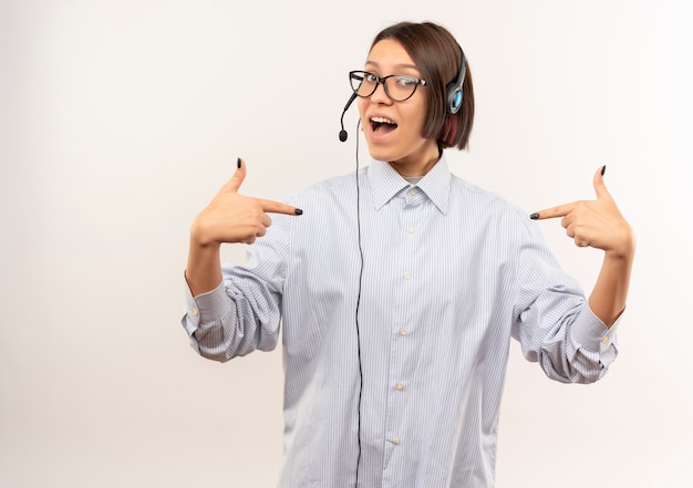 Onder de indruk jong call centreermeisje die glazen en hoofdtelefoon dragen die op zichzelf richten dat op wit met exemplaarruimte wordt geïsoleerd