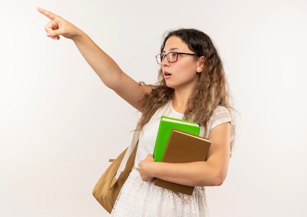 Onder de indruk jong mooi schoolmeisje die glazen en achterzak dragen die boeken wijzen en naar geïsoleerde kant kijken kijken