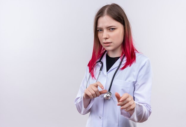 Onder de indruk jonge artsenvrouw die stethoscoop medisch kleed draagt, hand in hand rond maag op geïsoleerde witte muur met exemplaarruimte