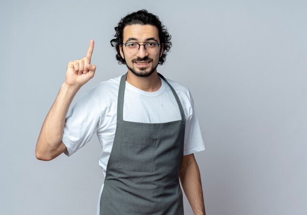 Onder de indruk jonge blanke mannelijke kapper draagt ?? een bril en golvende haarband in uniform verhogen vinger geïsoleerd op een witte achtergrond met kopie ruimte