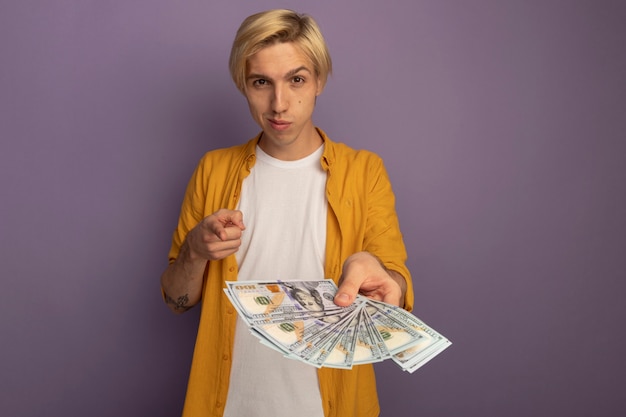 Gratis foto onder de indruk jonge blonde kerel die een geel t-shirt draagt dat je gebaar toont en contant geld uitstelt