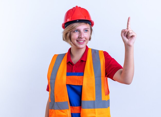 onder de indruk jonge bouwvrouw in uniforme punten naar boven geïsoleerd op een witte muur