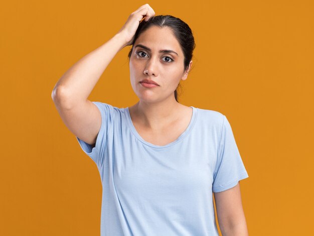 Onder de indruk jonge brunette blanke meisje legt hand op het hoofd geïsoleerd op een oranje muur met kopieerruimte