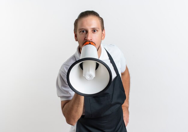 Onder de indruk jonge knappe kapper uniform praten door spreker met hand op taille geïsoleerd op wit met kopie ruimte dragen