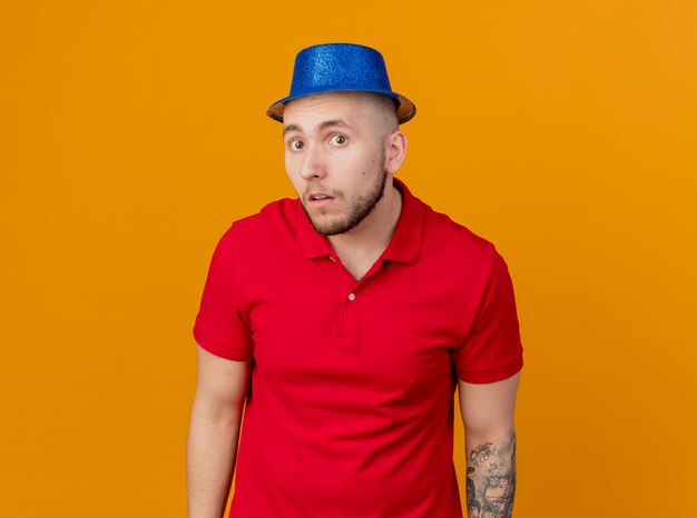 Onder de indruk jonge knappe Slavische feestmens met feestmuts kijken naar camera geïsoleerd op een oranje achtergrond met kopie ruimte