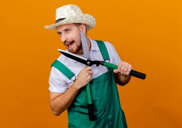 Onder de indruk jonge knappe Slavische tuinman in uniform en hoed met snoeischaren kijken naar geïsoleerde kant