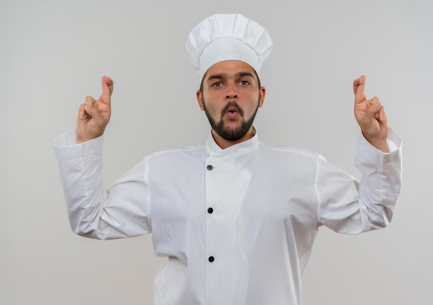 Gratis foto onder de indruk jonge mannelijke kok in uniform van de chef-kok doet gekruiste vingers gebaar geïsoleerd op een witte muur