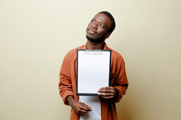 Onder de indruk kijkend naar kant jonge Afro-Amerikaanse man met klembord geïsoleerd op een witte achtergrond