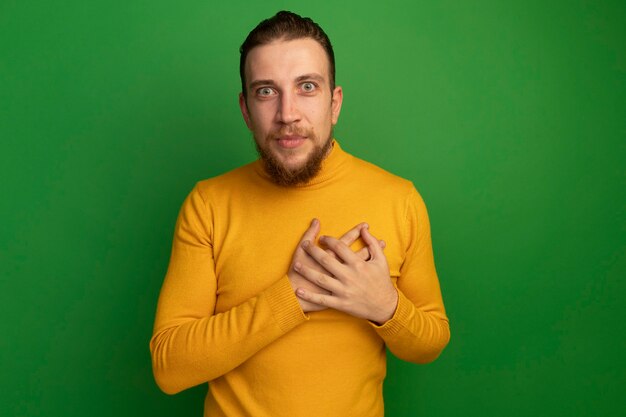 Onder de indruk knappe blonde man legt handen op de borst op groen